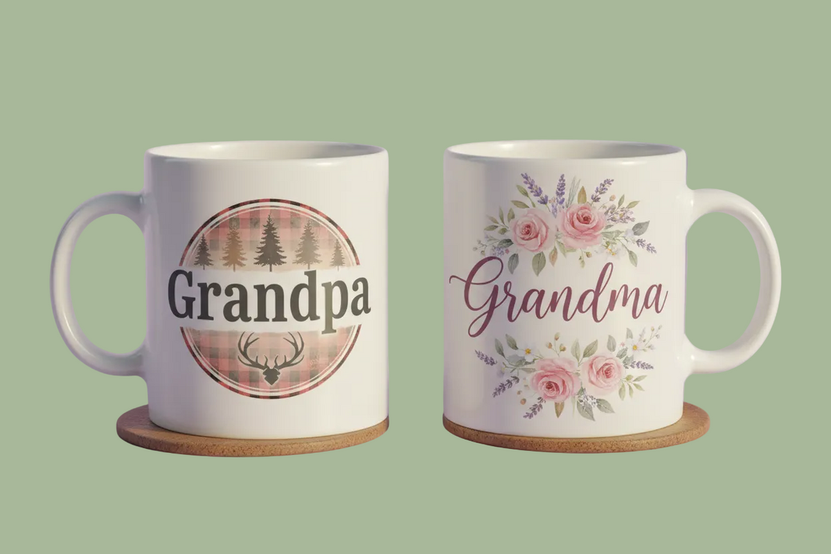 Two white ceramic mugs with custom names, 'Grandpa' and 'Grandma', displayed side-by-side on cork coasters against a lavender background. The 'Grandpa' mug features a pine tree and deer graphic on a plaid background, while the 'Grandma' mug has a pink floral design.